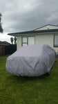 grey car cover on car with white house 